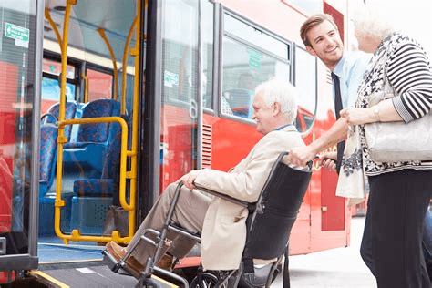 A man on a wheelchair being assisted onto a bus