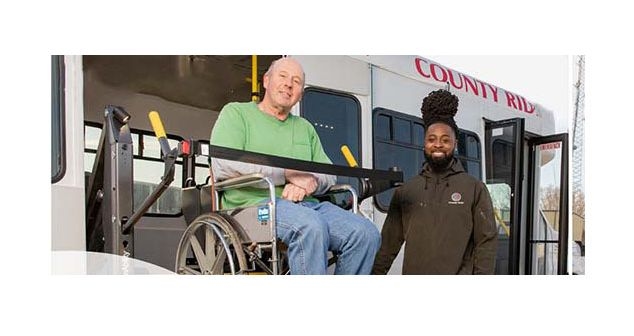 A man on a wheelchair being assisted off of a bus